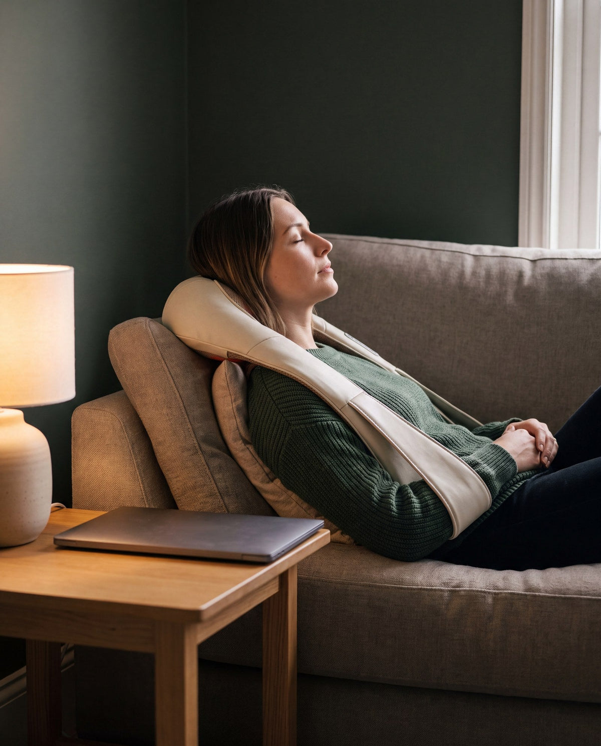 A woman relaxing on a sofa wearing the heated neck and shoulder massager